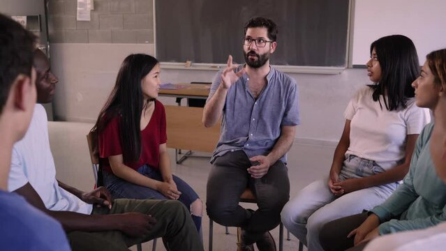 Multicultural group of undergraduate students sitting in chairs forming a circle chatting and interacting during the presentation of Caucasian teacher. Educational concept in generation z.