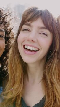 Portrait of three smiling young diverse women having fun together on city street. Happy female friends enjoying day off at weekend over urban background. Friendship concept. Vertical video.