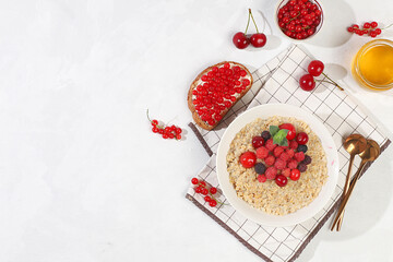 Healthy breakfast with ingredients, oatmeal pudding or porridge with raspberries, cherries, currants, honey and toast on a sunny table. The concept of healthy and natural food, lifestyle,