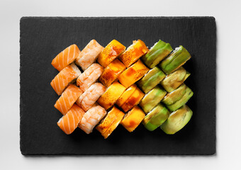 Set of colorful rolls with shrimp, salmon, avocado, cheese on a black stone plate, top view.