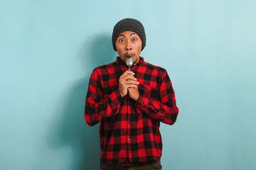 Surprised Young Asian man with beanie hat and red plaid flannel shirt holding a spoon near his...