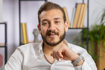 Naklejka premium Portrait of happy smiling bearded middle eastern businessman at modern home office workplace desk looking at camera. Male in formal shirt. Man guy remote distant online working on laptop