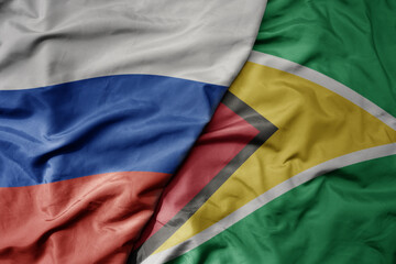 big waving realistic national colorful flag of russia and national flag of guyana .