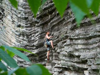 Pretty tourist rock climbing up the picturesque rocky wall with basalt columns