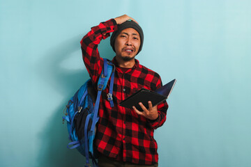 A regretful young Asian student with beanie hat and red plaid flannel shirt, wearing a backpack, is...