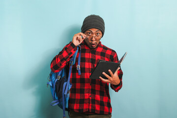 A surprised young Asian student in a beanie hat and a red plaid flannel shirt, wearing a backpack...