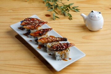 Close-up shot of a white dish of unagi sushi set, Japanese food serving on the clear white table with japanese tea cup and many japanese stye decoration in background