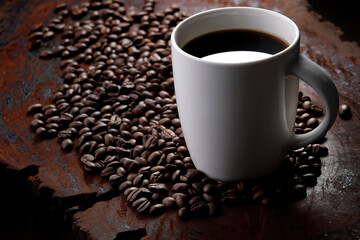 black coffee in white mug with surrounded by roasted coffee beans on dark red wood table