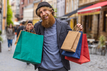 Happy smiling stylish beardedman shopaholic consumer after shopping sale with full bags with gifts...