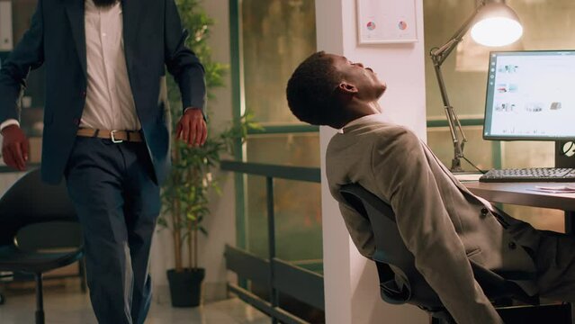 Accountant catching coworker asleep in desk chair after working all night, waking him up in playful manner. Happy employee messing with sleeping coworker, playing jokes on him