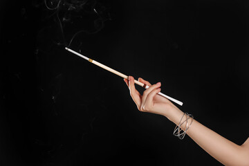Woman holding long cigarette holder on black background, closeup