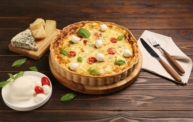 Delicious quiche with mozzarella cheese, tomatoes and basil on wooden table