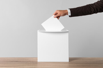Man putting his vote into ballot box on light grey background, closeup - obrazy, fototapety, plakaty