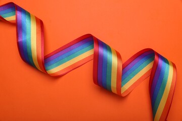 Rainbow ribbon on orange background, top view. LGBT pride