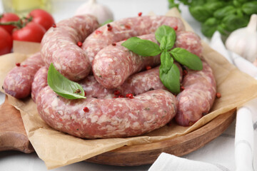 Raw homemade sausages, basil leaves and peppercorns on table, closeup