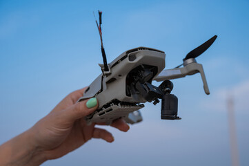 Woman holding crashed drone against blue sky. 