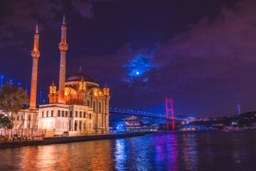 Fototapeta na wymiar Ortaköy, İstanbul-Mosque and Bosphorus Bridge during blue hour, full moon and blue night Sky. One of the most popular locations on the Bosphorus, Istanbul, Turkey, Selective Focus.