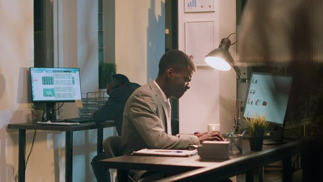 African american accountant exasperated with noisy colleague listening to music and pretending to beat drums during nightshift. Employee annoyed by distracting coworker banging desk in office