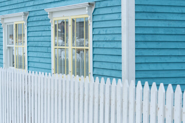 Two double hung windows with yellow trim on a blue exterior wall of a vintage style building. The...