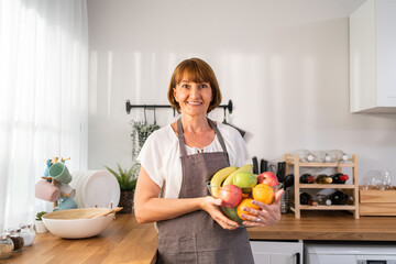 Portrait of Caucasian elderly woman hold fruit bowl and look at camera. 