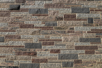 Full frame texture background of a modern ashlar masonry style multi-color granite stone wall, with blocks in varying sizes and shades of white, brown, red and blue