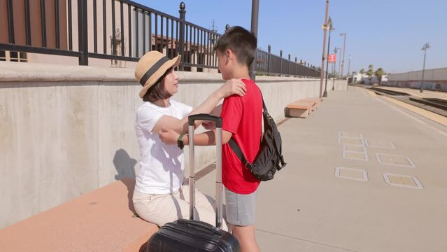 Mother and son at the train station with her suitcase.
