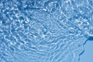 Blue water with ripples on the surface. Defocus blurred transparent blue colored clear calm water surface texture with splashes and bubbles. Water waves with shining pattern texture background.