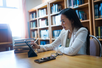Female university lecturer working in library with a tablet and books on table