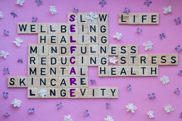 Top view of SELFCARE word on pink background with flowers. Minimalism creative crossword puzzle...