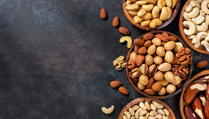 Assortment of nuts in wooden bowl on dark stone table. Cashew, hazelnuts, walnuts, almonds, brazilian nuts and pine nuts. Top view with copy space.