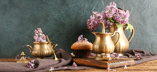 Lilac flowers with dishes and cupcake on wooden table