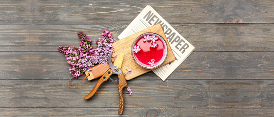 Cup of tea with lilac flowers, newspaper and gardening pruners on wooden table, top view
