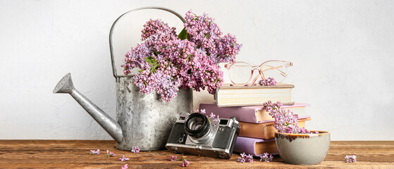 Composition with watering can, old photo camera, books and lilac flowers on wooden table