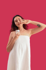 Fototapeta premium Young brunette woman with jar of cosmetic cream on pink background