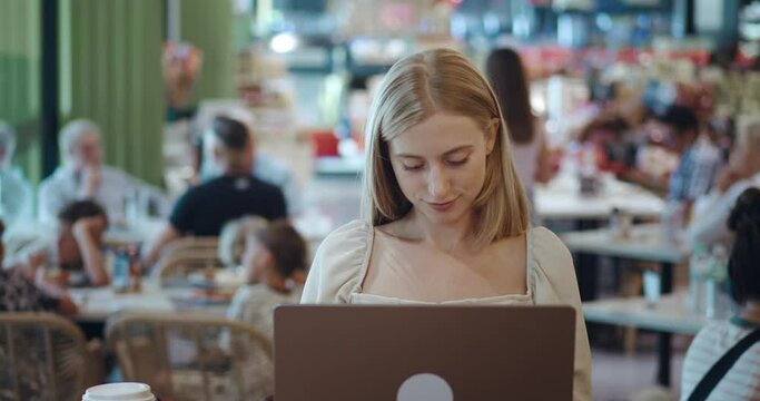 businesswoman with blond hair sits at a computer in a cozy cafe working self employment. businesswoman has her own small business remotely. concept self employment. drinks coffee,female checking sales