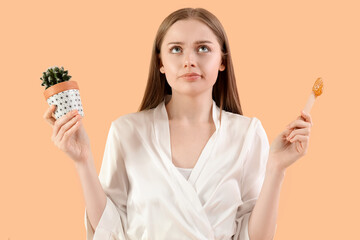 Thoughtful young woman with sugaring paste and cactus on beige background