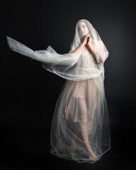 Naklejka premium Full length portrait of beautiful woman wearing white gown dress with flowing ghostly veiled fabric, isolated on dark studio background.