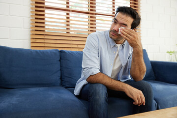 young man feeling upset, crying and holding tissue paper on sofa