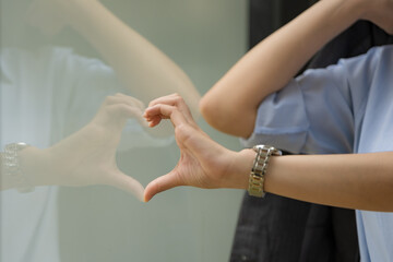 Fototapeta premium Close-up hand of Asian businesswoman to heart shape with window glass.