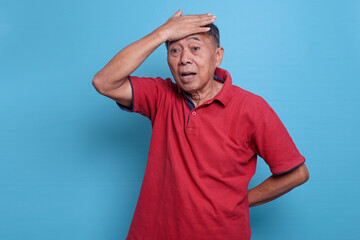 Forgetful elderly senior man in red t-shirt, touching his head feels desperately as forgets about...