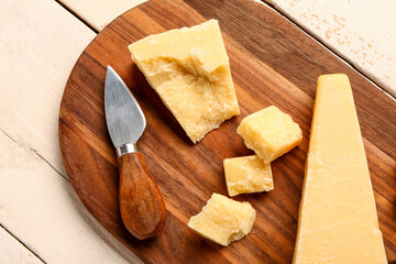 Board with pieces of tasty Parmesan cheese on light wooden background, closeup