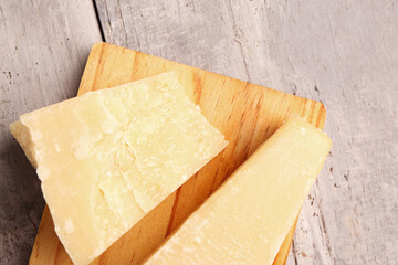 Board with pieces of tasty Parmesan cheese on light wooden background, closeup