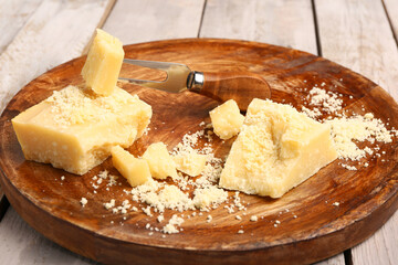 Plate with pieces of tasty Parmesan cheese on light wooden background, closeup