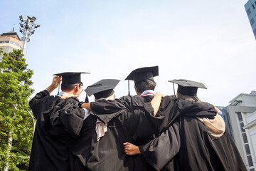 Rear view of young group of happy multiracial graduate friends hugging each other standing in a row...