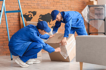 Male movers wrapping box with stretch film in room