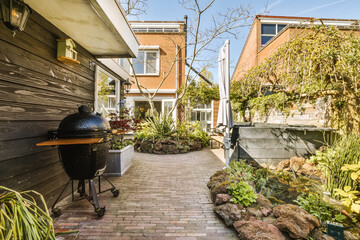 a back yard with some plants on the left side and a grill in the middle to the right, surrounded by brick pavers