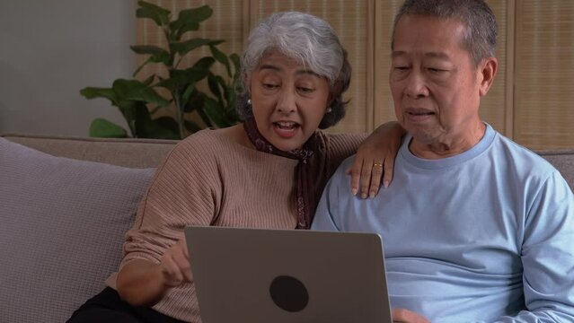Cheerful loving senior asian couple looking at the same laptop computer, having fun web surfing internet, shopping online or communicating