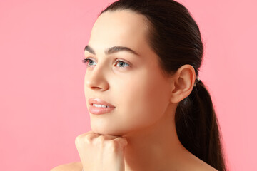 Young woman doing face building exercise on pink background, closeup