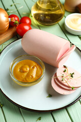 Plate with tasty boiled sausage and sauce on green wooden background