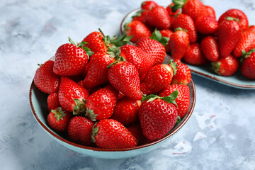 Bowl and plate with fresh strawberries on blue background
